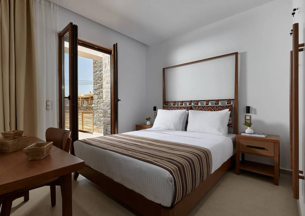 Double bedroom with striped woven bedspread, patterned headboard and doors opening to a stone courtyard