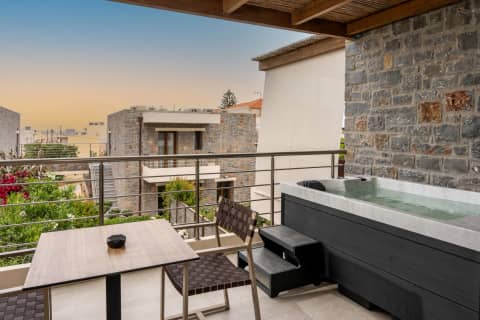 Balcony hot tub against a stone wall at sunset, with cafe table overlooking the gardens of Volta Stay