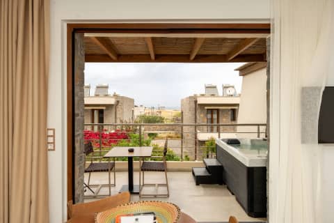 View through open glass doors to a furnished balcony with hot tub, bougainvillea and stone suites beyond