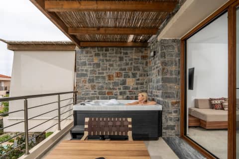 Guest relaxing in a balcony hot tub beneath a bamboo pergola, framed by rough stone walls