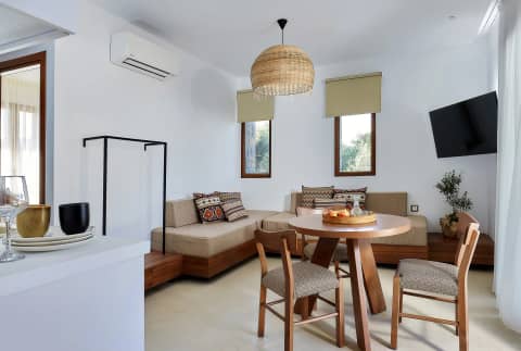 Living area with corner sofa, round wooden dining table, rattan pendant and small garden-view windows