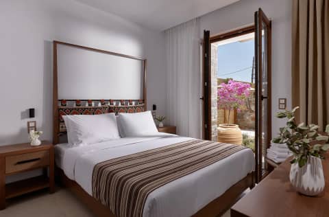 Double bedroom with striped bedspread and open door to a courtyard with blooming bougainvillea in Gouves, Crete