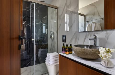 Marble-tiled bathroom with walk-in shower, stone basin and local toiletries on a wooden vanity