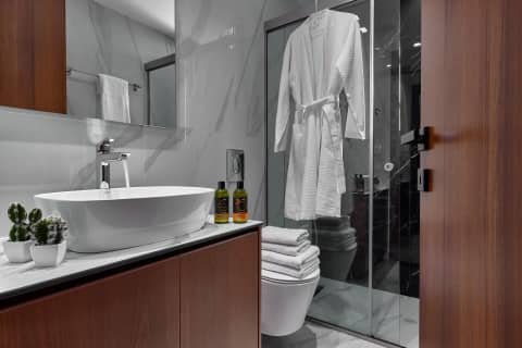 Modern bathroom with white basin, walnut cabinetry, glass shower and a hanging white bathrobe