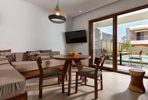 Living room with corner sofa and dining table, glass doors framing the garden and private pool