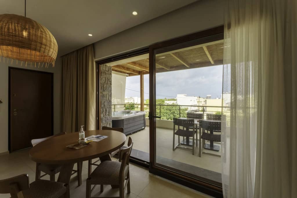 Dining area with rattan pendant lamp opening to a covered balcony with hot tub and views over Gouves, Crete