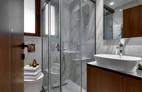 Modern bathroom with marble-look tiles, glass walk-in shower, white basin and towels