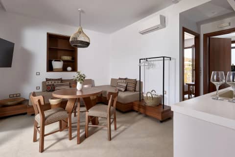 The open plan living room of a one bedroom suite with corner sofa, round dining table and clothes rail