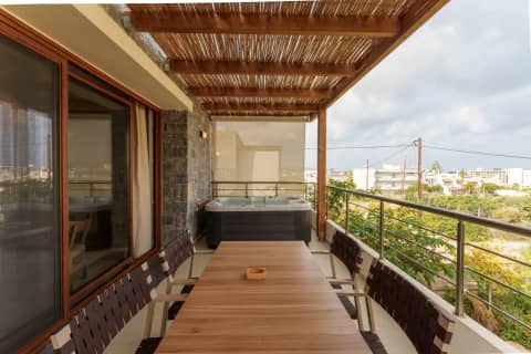 Long wooden dining table on a bamboo-shaded suite terrace with hot tub and railing views over Gouves, Crete