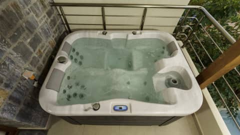 Overhead view of a four-seat hydromassage hot tub with headrests on a balcony beside a stone-built wall