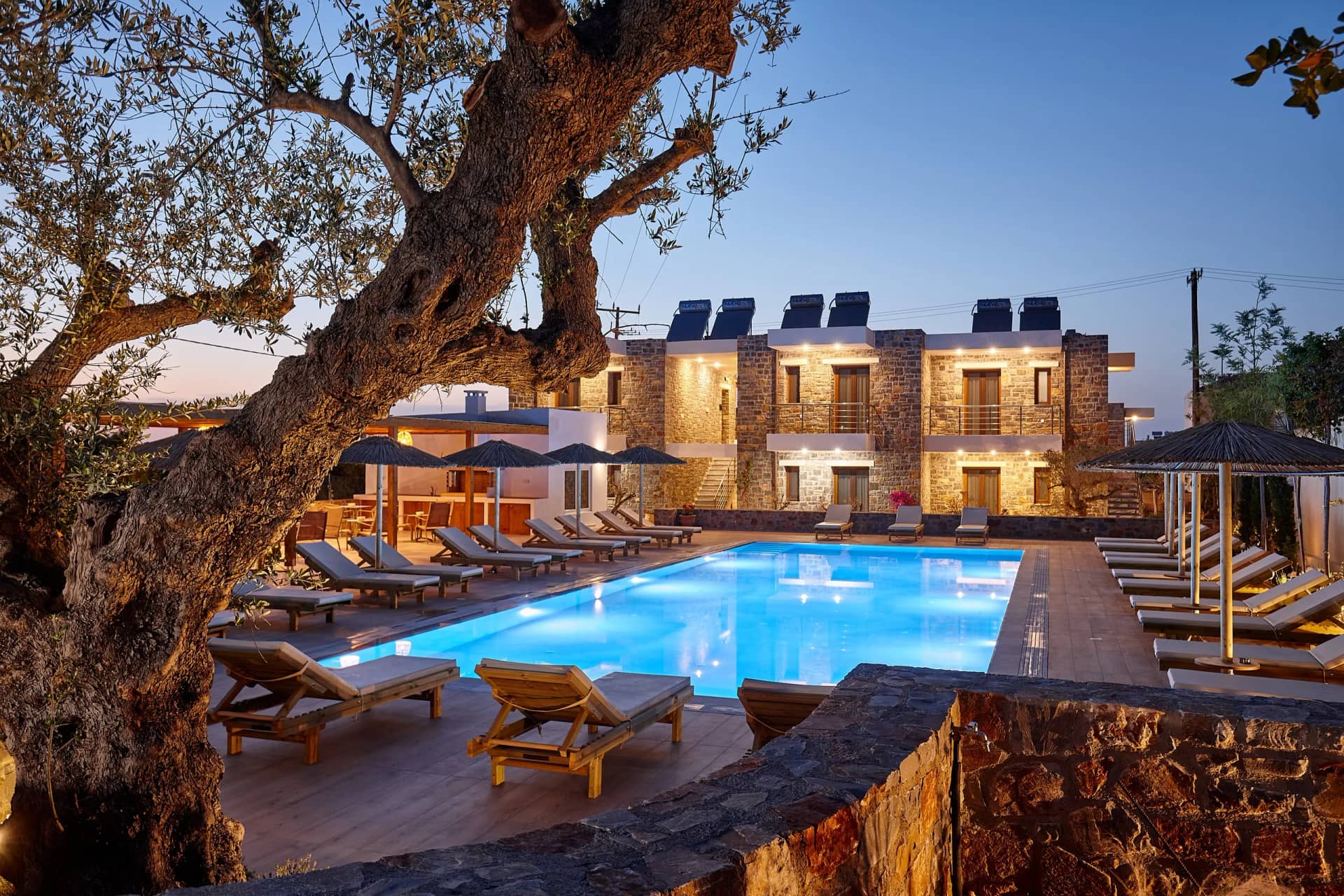 Evening at Volta Suites and Villas: the pool under the old olive tree, stone buildings glowing behind