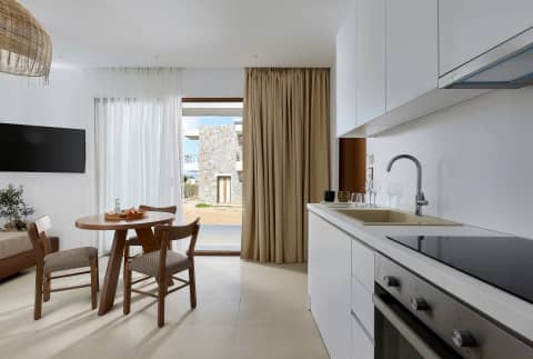 One-bedroom suite kitchenette and dining table with doors opening to a private terrace and stone-built views