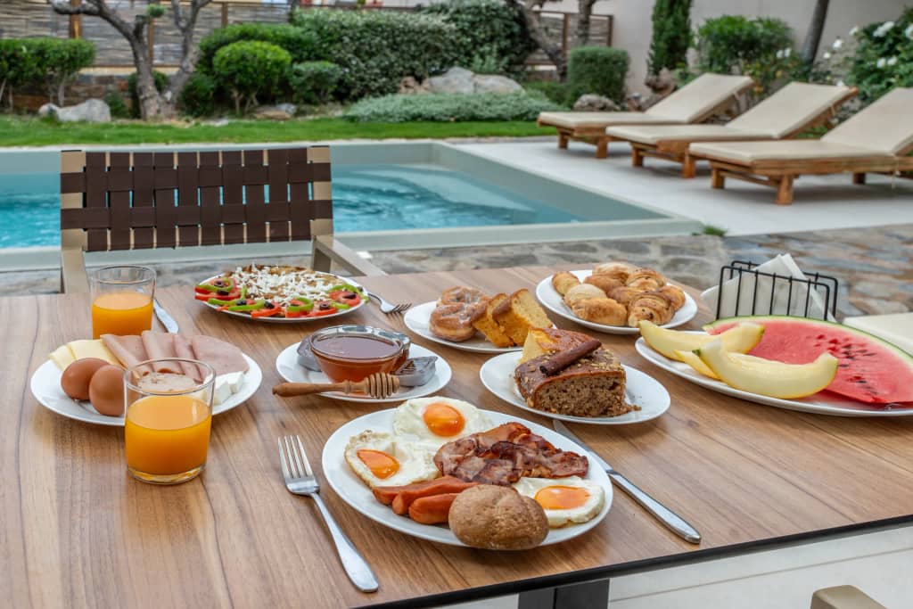 Breakfast plates with fried eggs, cold cuts, fresh bread and watermelon served at a poolside table at Volta