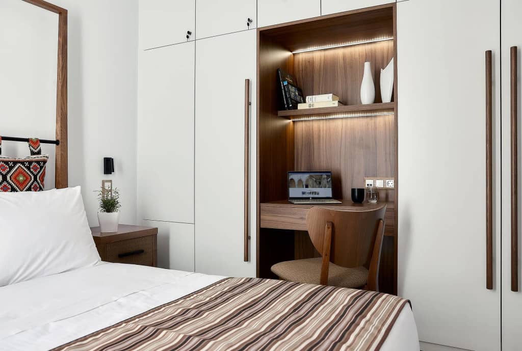 Bedroom with double bed and a lit walnut desk niche with books and workspace